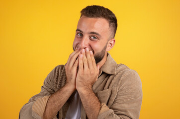 Laughing glad millennial caucasian guy with beard in casual covers mouth with hands, has fun