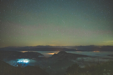 Mer de nuages en montagne avec un ciel étoilé et les lueurs des villages sous la couche épaisse de cette couette de coton