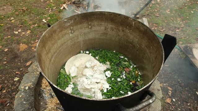 Green beans ends or trims and egg shells and other food leftovers being cooked in large pot over fire pit while preparing animal feed.