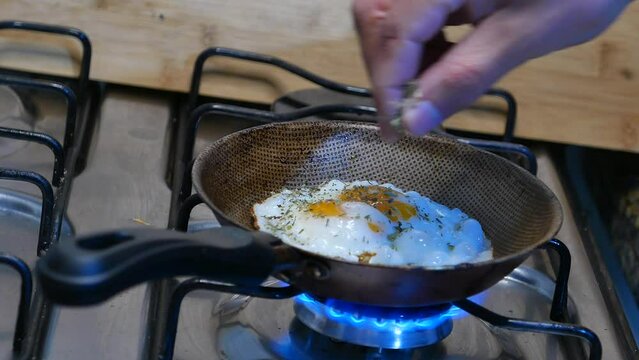  POV: person adding oregano to fried eggs. Frying an egg with double yolks. Fried eggs in a skillet. Double eggs. Double fried eggs. Making fried eggs in a frying pan. Pouring oregano into fried eggs.