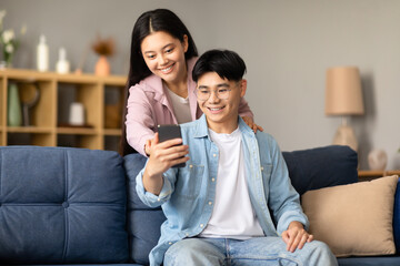 Smiling Korean couple using smartphone in modern living room