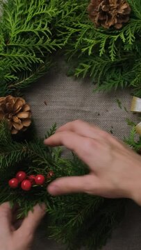 Vertical video. Female hands decorating Christmas wreath. DIY Xmas flower arrangement. 