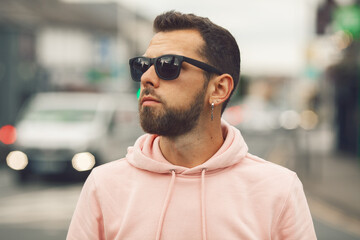 City lover concept. Close up portrait of fashionable young man with beard wearing sunglasses, pink...