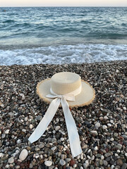 Woman's straw beach hat on the pebble seashore. Beautiful sunny day. Vacation, Summer concept