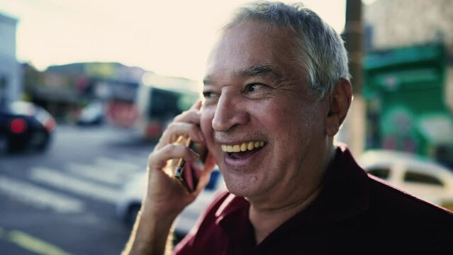 Happy Elderly Caucasian Man Speaking on Phone in Urban South American Setting with sunlight flare shining in backlight