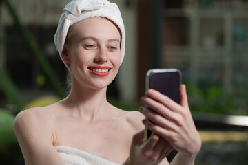 Portrait of close up beautiful caucasian woman in white towel taking video of calm and relaxing nature by using her mobile phone. Pretty girl with beautiful skin take photo. A Side view. Tranquility.