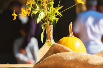 Yellow pumpkin in warm sunny autumn light. Nearby is a vase of yellow flowers.