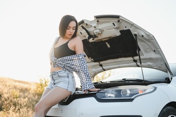 The young girl broke the car and she opened the hood and tried to repair the car on the road. A woman calls on a smartphone with a car evacuation service