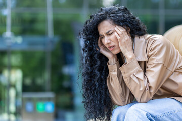 Mature adult woman depressed and with headache sitting on bench outside office building, overworked and overworked business woman sad, after work.