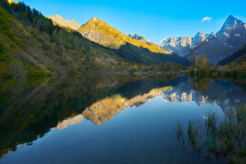 Autumn. A picturesque mountain lake with clear water surrounded by mountains. Mountain relief and blue sky are reflected in the water. Copy space.