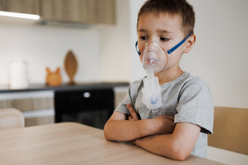 Sick little boy making inhalation with nebulizer to reduce coughing at home, child taking medication while breathing in through face mask - obrazy, fototapety, plakaty