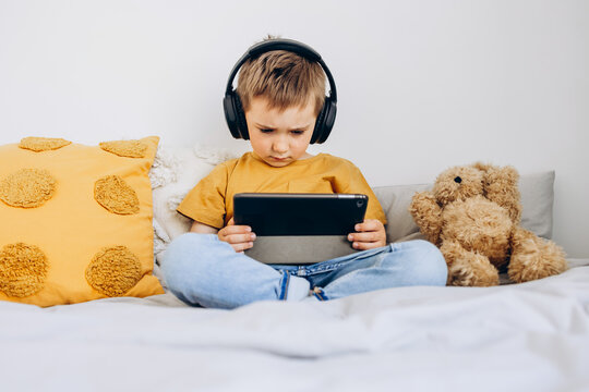 Toddler boy playing with digital wireless tablet computer at home. Baby child growing with online applications. Child and electronic devices concept. Portrait of toddler with smartphone