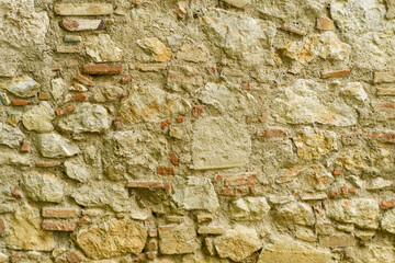 Old rough stone wall made of various square natural stones in beige, gray and brown colors.