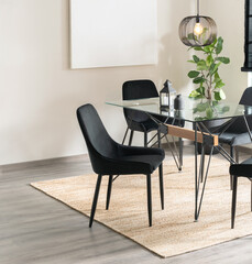Modern Dining Room with Black Fabric Dining Chairs, Rectangular Glass Top Table with Black Metal Legs, Blank Poster Mock-Up on the Wall, in a Bright Room with an Area Rug and Grey Wooden Flooring.
