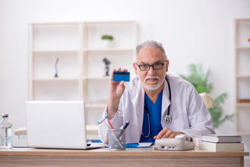 Old male doctor holding credit card
