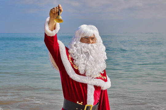 Santa Claus rings a bell at sea on a hot summer day. Xmas or New Year's vacation in hot countries. Santa's summer vacation. - Powered by Adobe