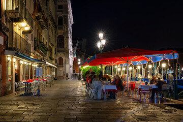 Grand canal with tables of restaurant in Venice, Italy. Architecture and landmark of Venice. Night cozy cityscape of Venice.