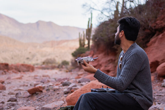 Young adult holding a drone before flying it over a desert landscape in northern Jujuy, Argentina. Photo with space for text.