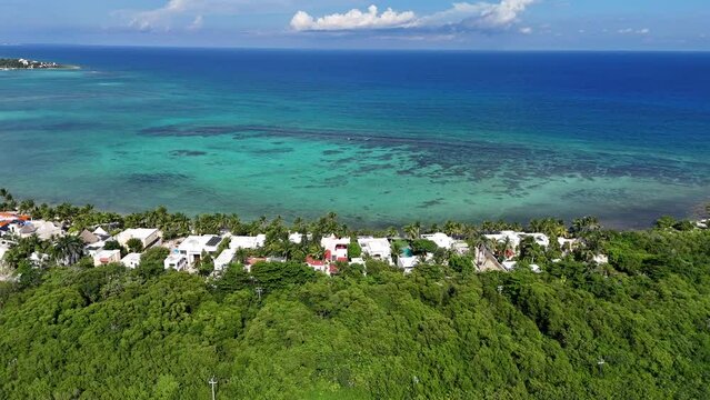 Drone aerial view of transparent blue Caribbean Sea with Cora reef and vacation houses surrounded by green vegetation along the coastline on a blue sky day in Tulum 