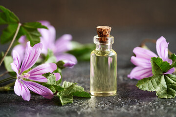 A bottle of essential oil with fresh common mallow