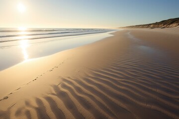 A serene beach scene with golden sand, shimmering sea, and long shadows cast by the early morning sun. Generative AI