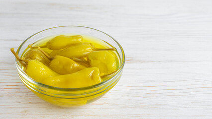 Pickled yellow pepper, pepperoncini or friggitelli in bowl on white wooden background. Hot pepper marinated, brined. Traditional Italian and greek cuisine, ingredient for salad, pasta, sauce.
