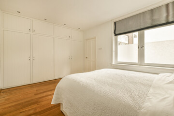 Fototapeta na wymiar a bedroom with wood flooring and white cupboards on either side of the bed in front of the window