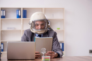 Old male employee wearing spacesuit in the office