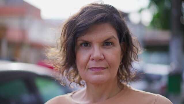 One mature woman with neutral serious expression close-up face standing on sidewalk, looking at camera