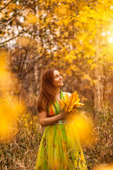 Portrait of lovely happy lady in yellow colored dress in fall forest, smiling looking up away. Stylish perfect woman model in natural autumn park of nature. Golden autumn concept. Copy ad text space