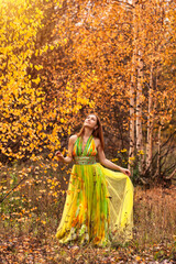 Full length of smiling lovely lady in yellow colored dress posing in autumn park outdoors, smiling looking up. Perfect woman model in natural fall nature. Golden autumn concept. Copy ad text space