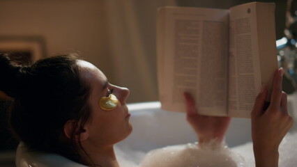Spa model reading book chilling foam bath closeup. Woman enjoying hot bathtub
