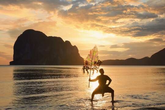 Silhouette of a man performing Traditional Thai Shadow Puppet Show on beach at sunrise, Thailand