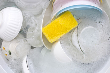 Dishes and bowls in water and bubbles of dishwashing liquid. Kitchen work