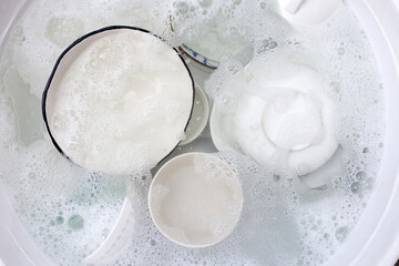 Dishes and bowls in water and bubbles of dishwashing liquid. Kitchen work