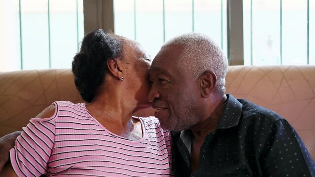 Senior couple kiss in loving relationship. A black wife elderly woman kissing a senior African American husband on cheek sitting on couch