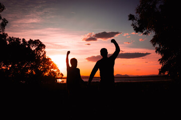 silhouette of father and son against nature background with raised hands,concept of family success