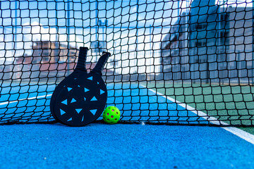 pickleball ball and paddles resting on the net of a pickleball court