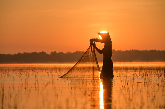 Silhouette of a fisherman standing in a river ready to throw a fishing net at sunset, Thailand