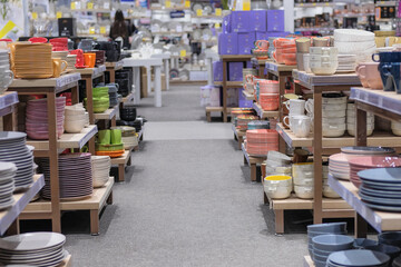 Rows of different multicolored cups, bowls and plates for home on shelves in a supermarket. Dishes...