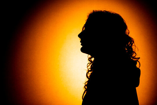 Silhouette of a young woman with long curly hair against an orange background