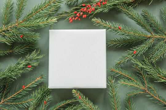 Overhead view of a white gift box surrounded by fir branches and berries