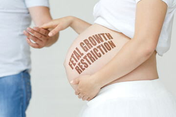 A pregnant woman holds her husband's hand on her stomach with the inscription - Fetal growth...