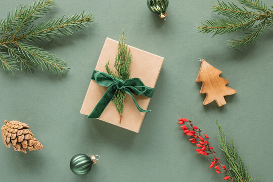 Overhead view of a wrapped gift box with Christmas baubles, fir branches, berries, a pinecone and wooden Christmas tree ornament