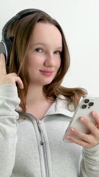 girl with headphones and a mobile phone at a photo shoot studio white background keep a finger on the headphones make eyes pose mobility music listen track sportswear play. sports