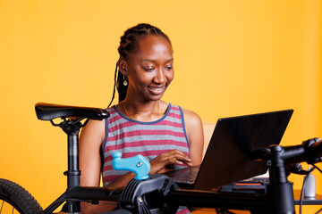 Dedicated african american female cyclist using laptop for research on bike maintenance....