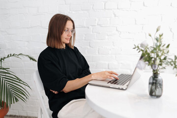 Smiling young woman in glasses holds online meeting via laptop. Businesswoman, entrepreneur,...