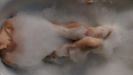Young lady relaxing foam bathtub top view. Relaxed woman washing body