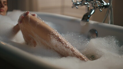 Carefree lady washing legs in foam bath closeup. Sexy woman touching body skin