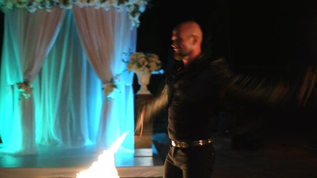 Male artist making a fire performance show with flame at festival at night. Artist juggling with burning fire fans near the hotel. Fire show performance with burning torch on the street.